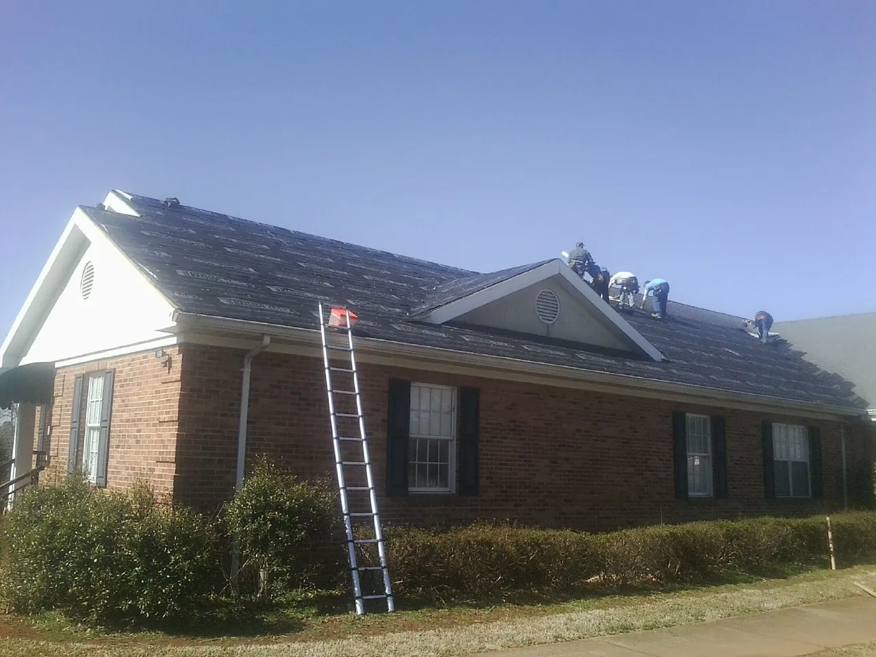 Crew tearing shingles off a brick ranch roof with a ladder set — Emergency Roof Repair work by our crew in Mayo